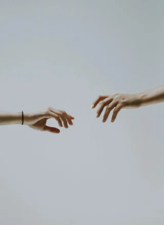 Two hands reaching toward each other against a plain background.